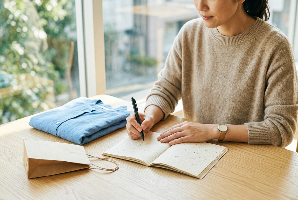 ノートとペンと服が置かれた机の前に座る女性